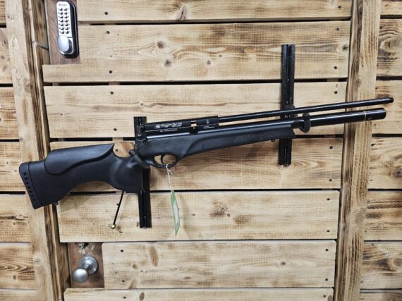 Black air gun mounted on a wooden wall with a textured finish and visible hardware.