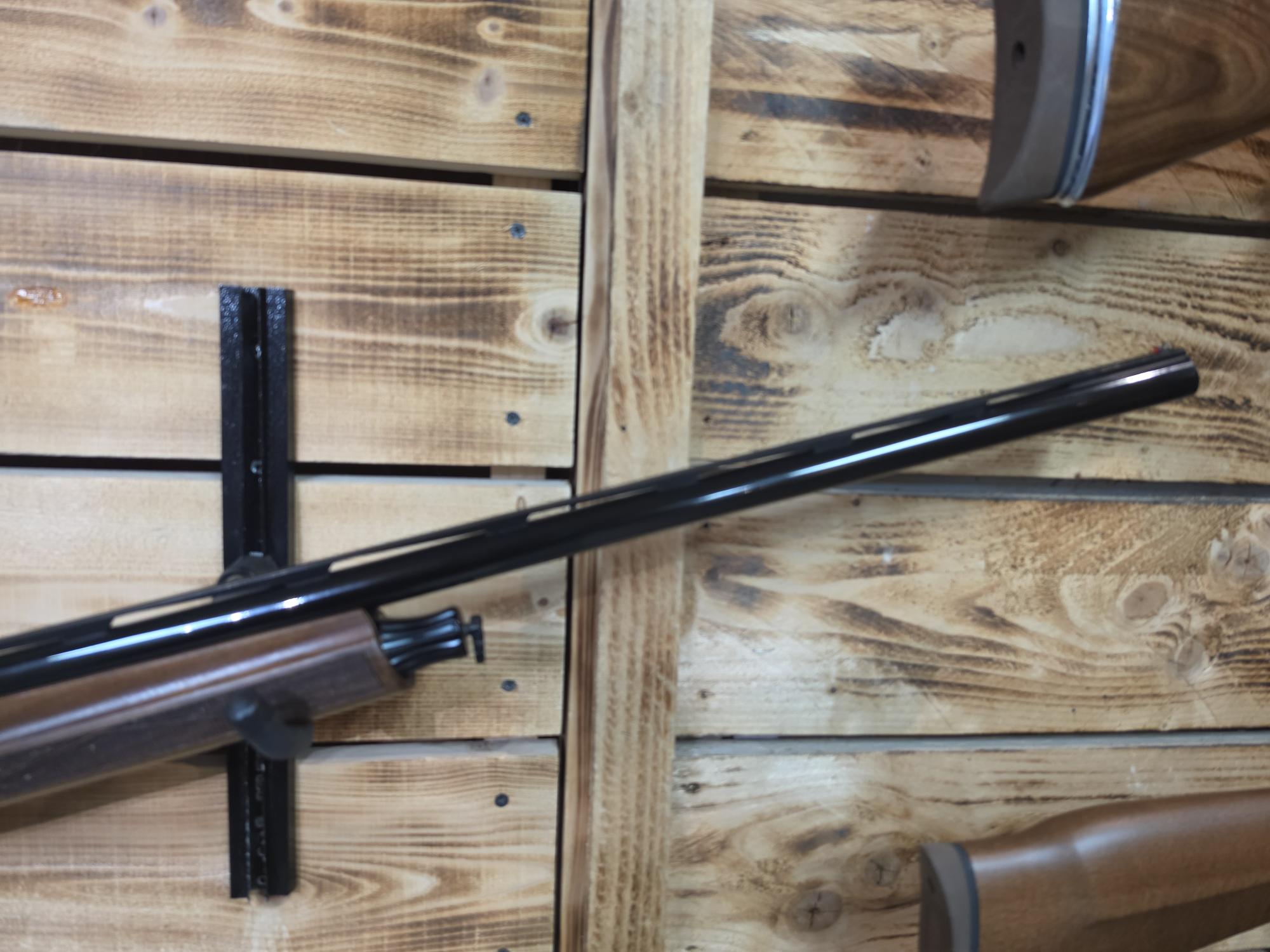 Wood-stocked Pre-Owned ATA Semi Auto 12 bore shotgun with a long black barrel displayed against wooden wall panels