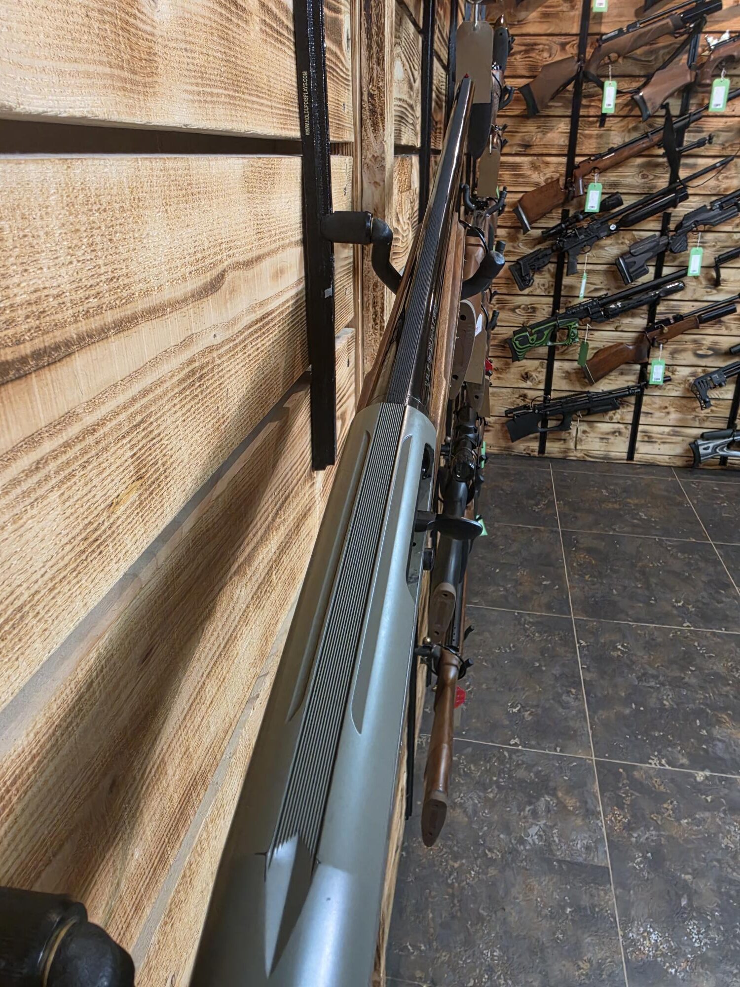 A silver and black Pre-Owned ATA Semi Auto shotgun rests on a wooden rack among other firearms at Crackshot.